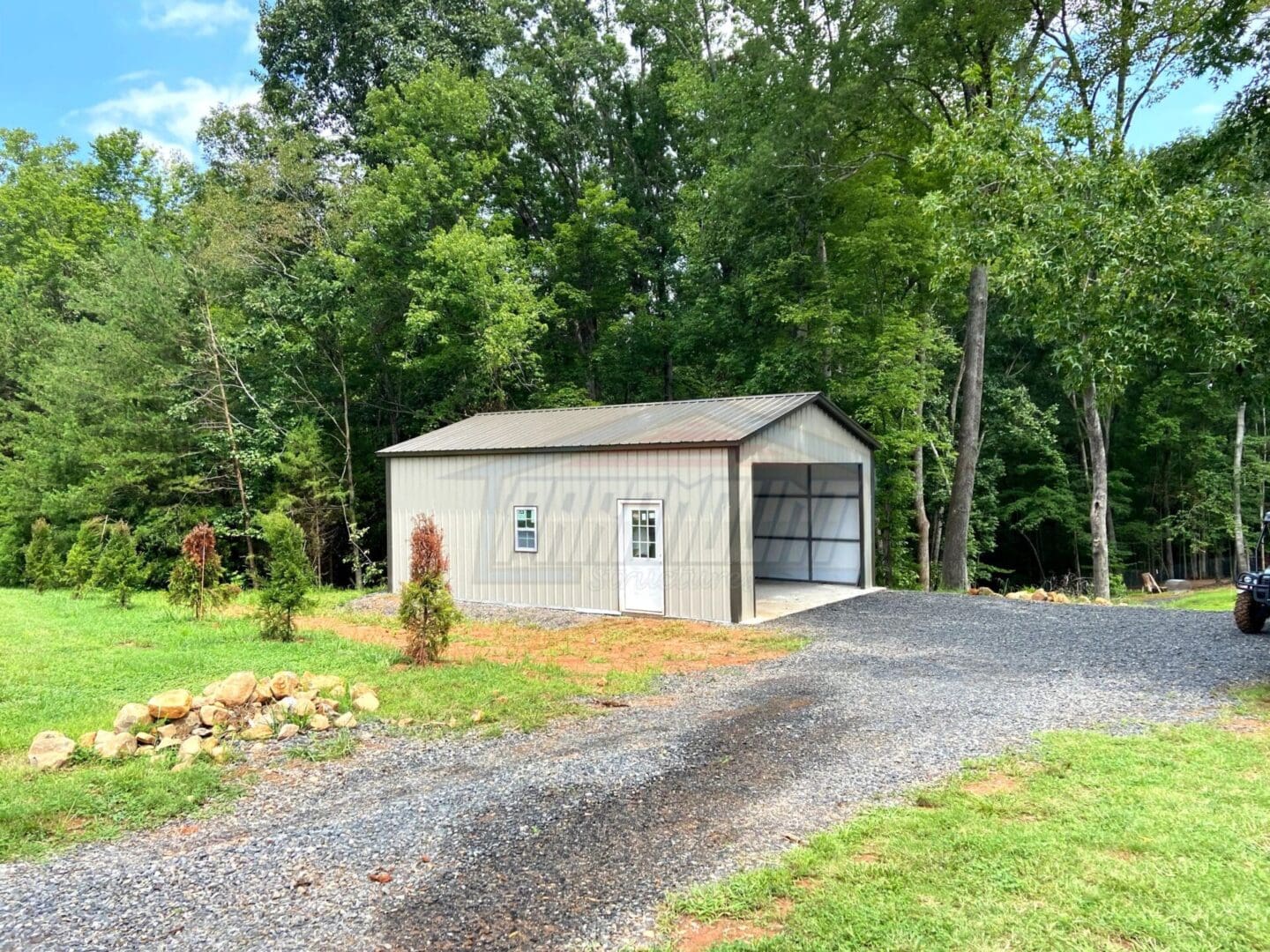 A small garage with a metal door and a gravel driveway.