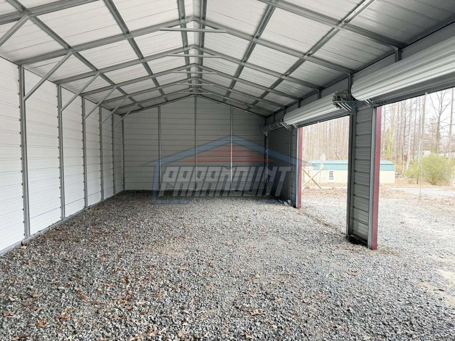 A metal building with two garage doors and a gravel floor.