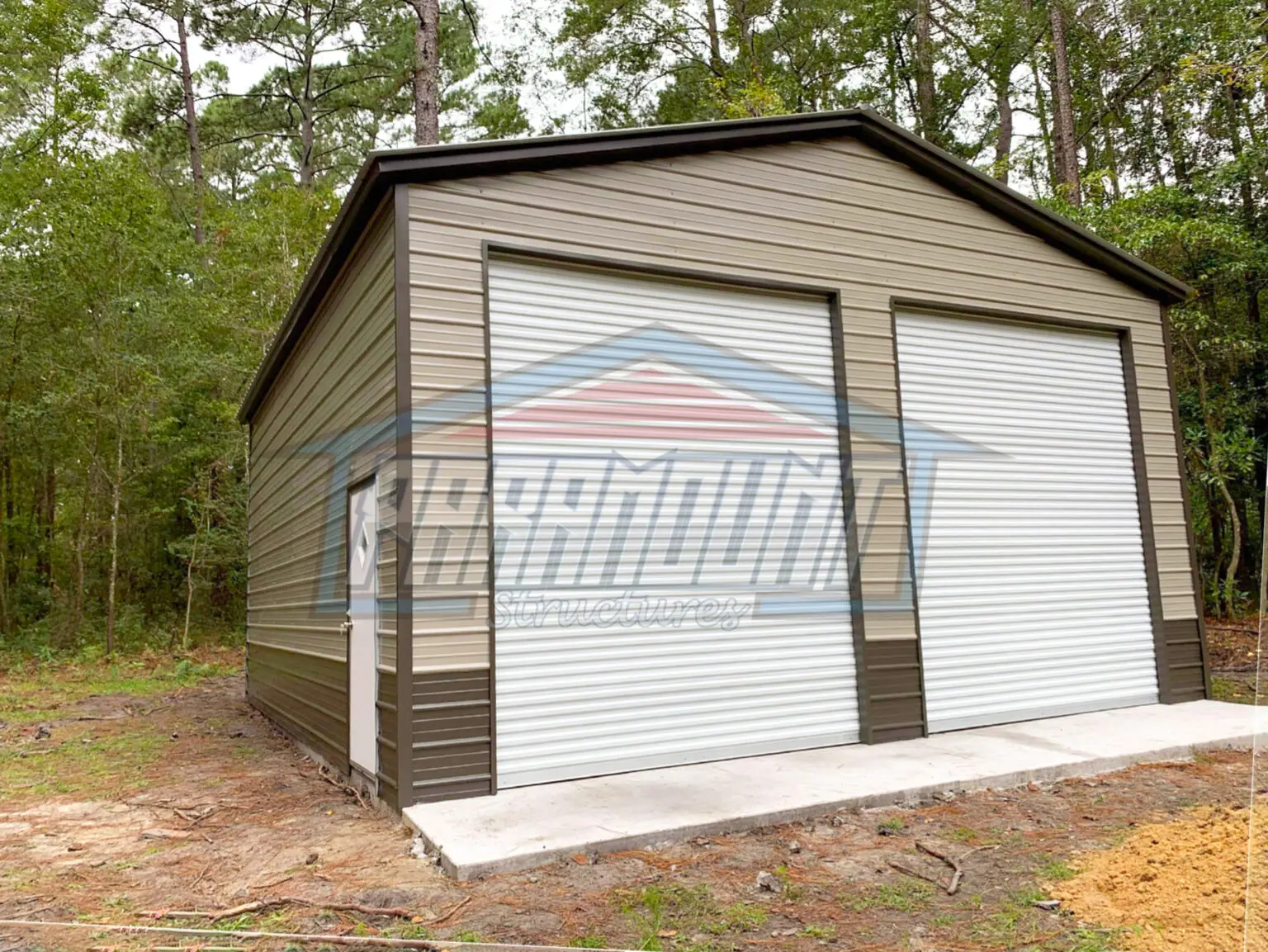 A brown and tan metal garage in the woods.